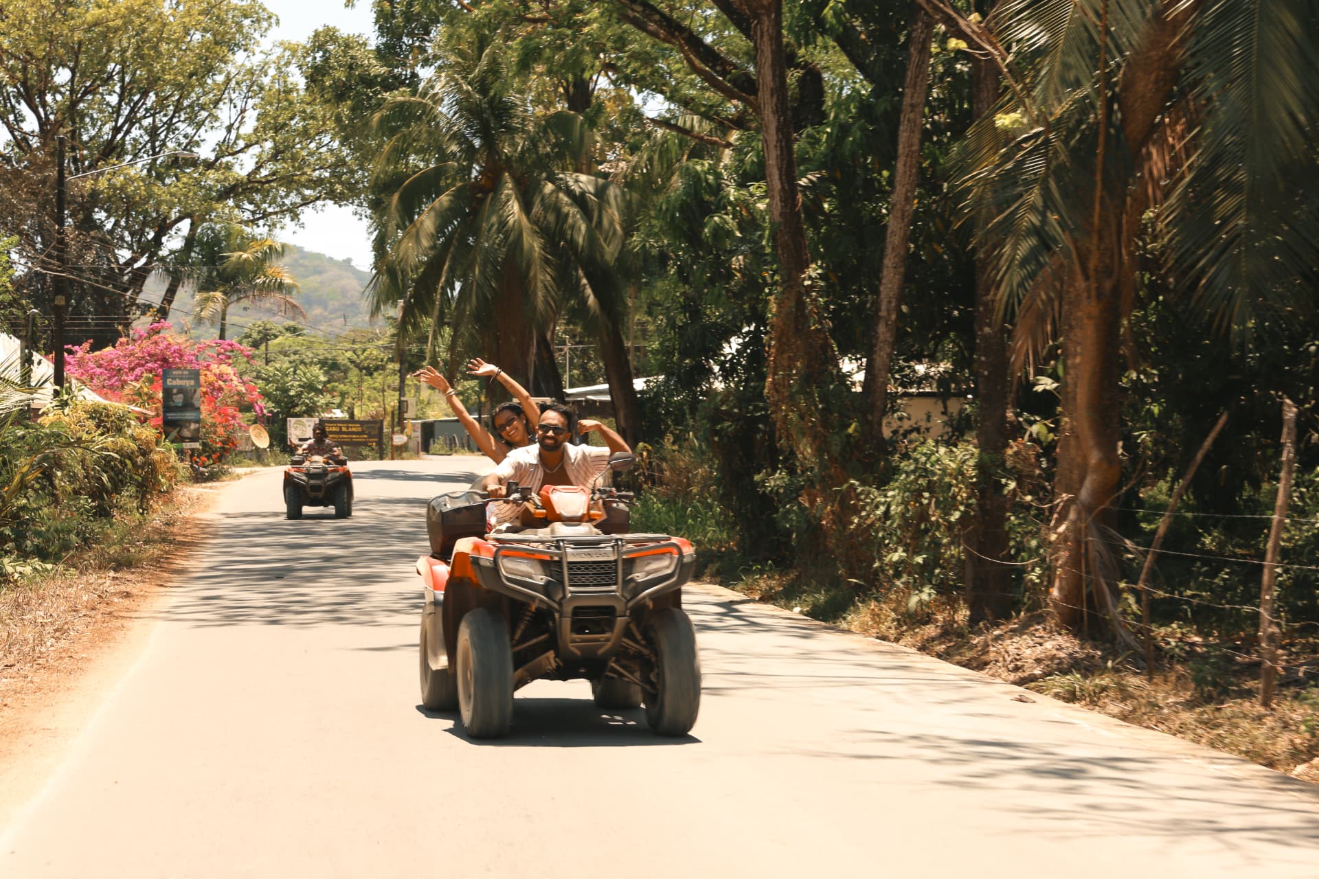 Two friends riding an ATV through the jungle, waving from the back
