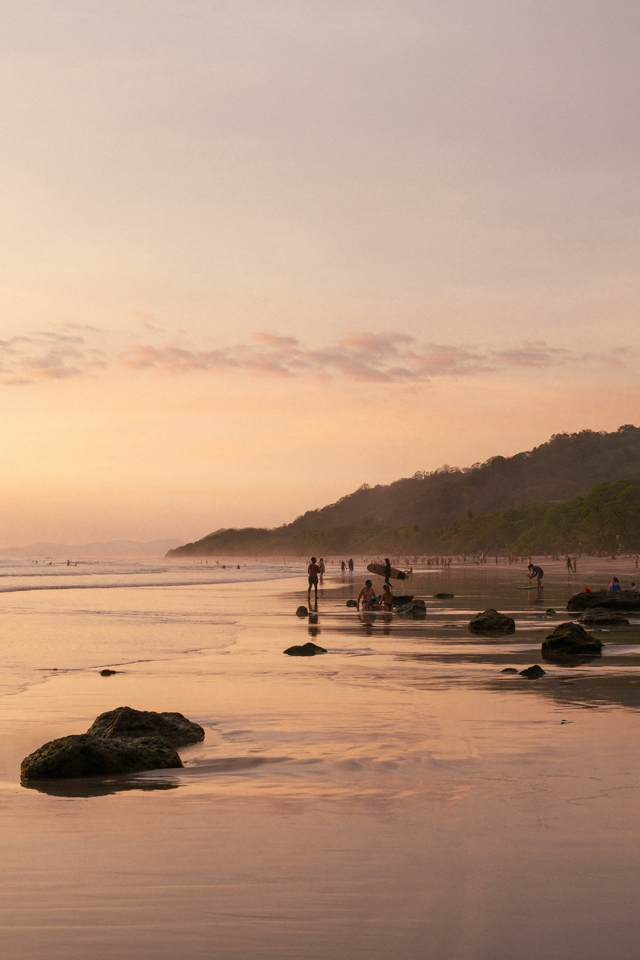Surfers walking the shoreline at sunset in Santa Teresa