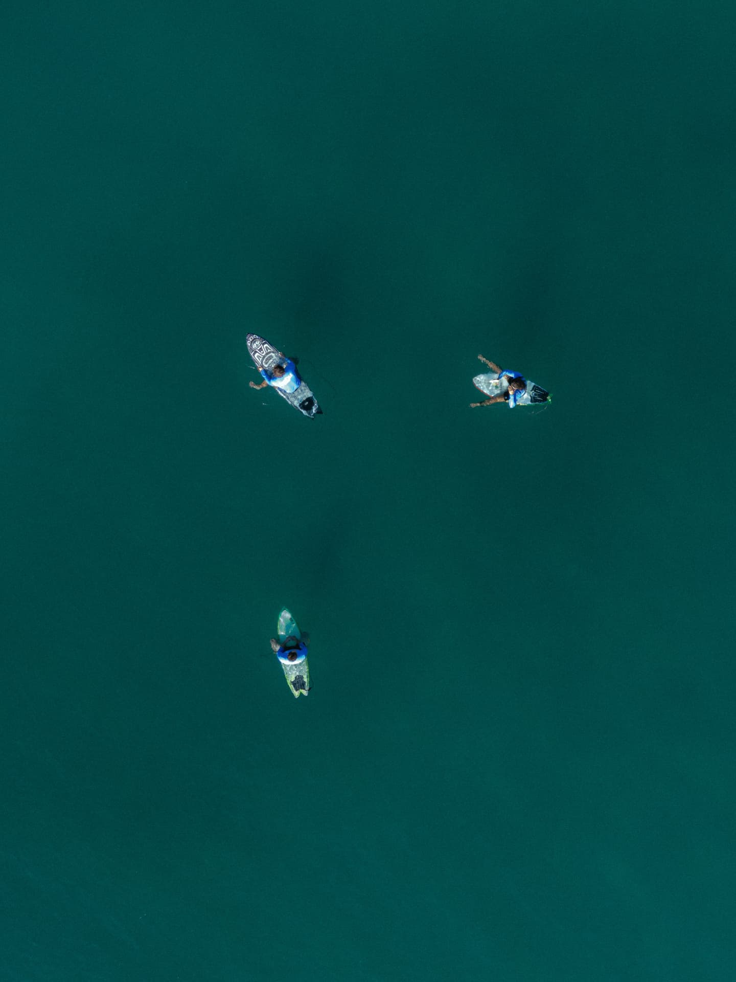 Aerial view of three surfers waiting for waves in clear water